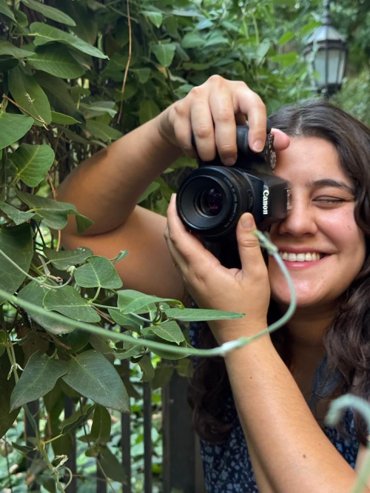 Lara Mateo smiling while shooting with her camera among green foliage